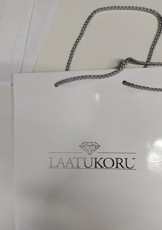 Laatukorun valkoinen paperikassi hopeafolioinnilla ja punotuilla kantonauhoilla